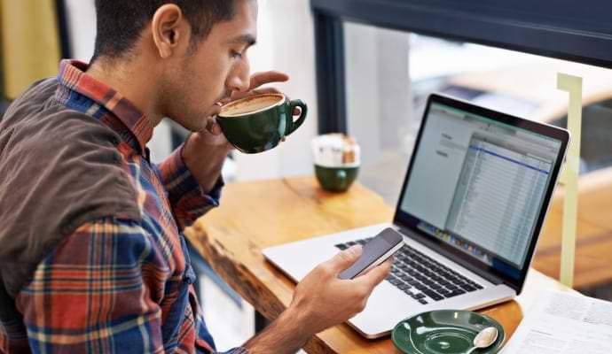 Man dricker kaffe medan han tittar på sin telefon.