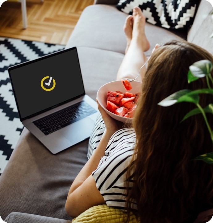 En kvinna som äter frukt med en bärbar dator vid sin sida som visar Norton LifeLock-symbolen.